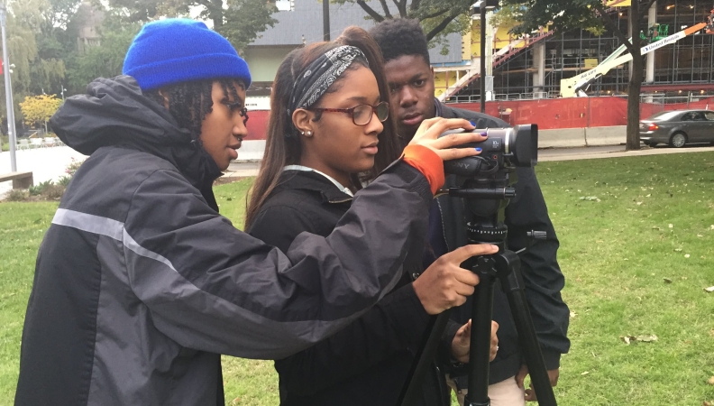 Three people adjusting a video camera in a park