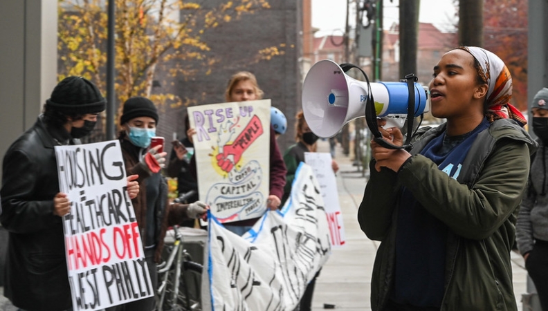 a person speaks into a megaphone while facing a group of people during a housing protest in West Philadelphia