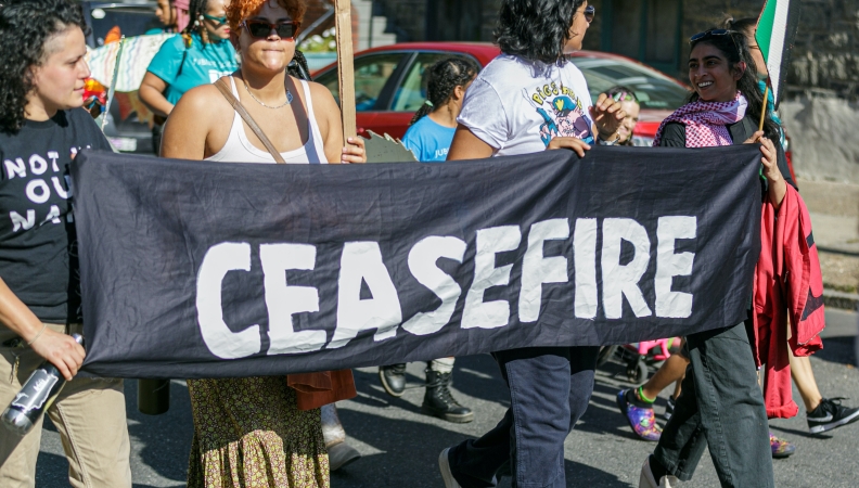a group of people at a protest hold a sign reading ceasefire