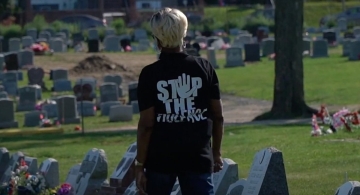 A person wearing a Stop The Violence black t-shirt looks at the graves in a cemetary