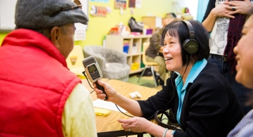 a woman holding a microphone to interview a person wearing a red vest