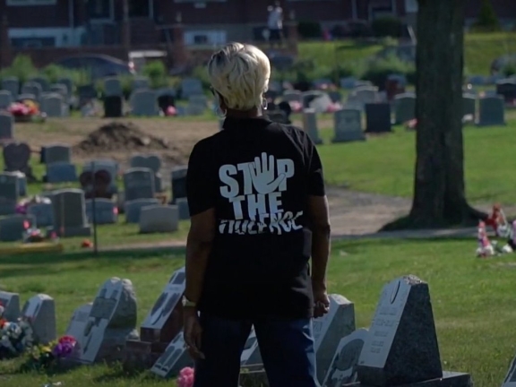 A person wearing a Stop The Violence black t-shirt looks at the graves in a cemetary
