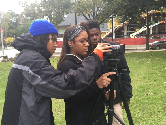 Three people adjusting a video camera in a park