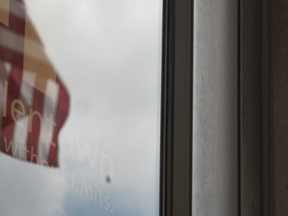 An exterior glass door with the reflection of an American flag and the words "Allentown City Without Limits" on it