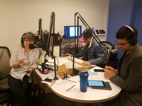 three people talking on microphones during the recording of a radio show