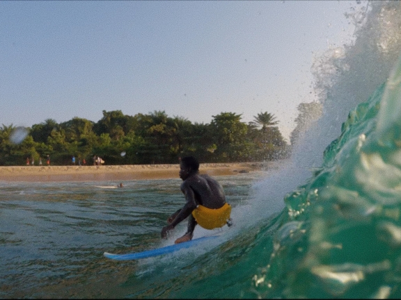 A person in yellow trunks surfing on a blue board with an island in the background