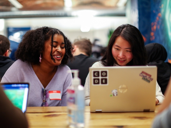 Two people seated at a table smiling at a laptop