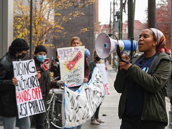 a person speaks into a megaphone while facing a group of people during a housing protest in West Philadelphia