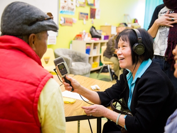 a woman holding a microphone to interview a person wearing a red vest