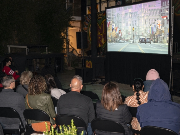 a group of people seated outdoors watching a movie screen 