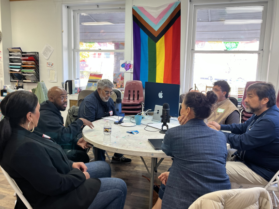 a group of people seated around a table recording a podcast episode