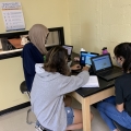 Three teenagers work on laptops at a desk