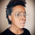 Profile view of a Black person with graying natural hair wearing glasses