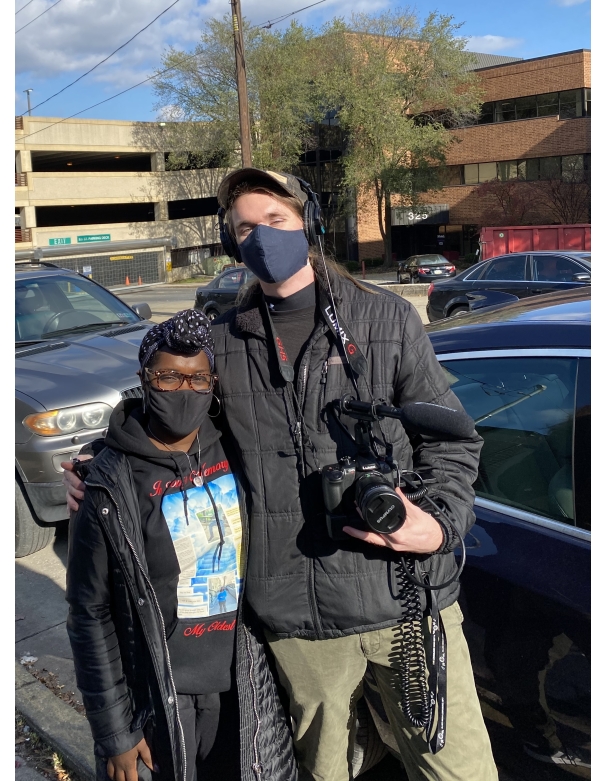 Two people hugging in a parking lot, one holding a camera