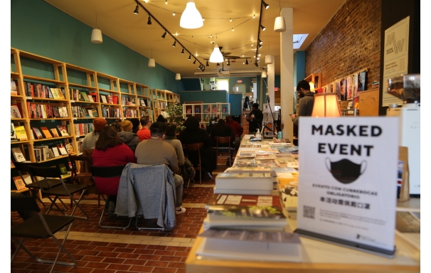 A group of people sitting on chairs in a bookstore with a sign saying Masked Event