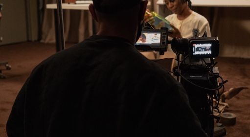 A film crew member looks through a viewfinder as an actor looks at something in their hands