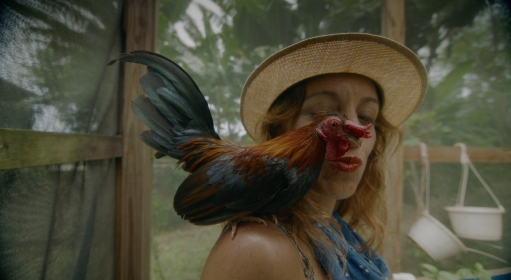 A person purses their lips towards a rooster perching on their shoulder
