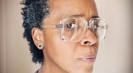 Profile view of a Black person with graying natural hair wearing glasses