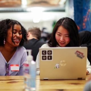 Two people seated at a table smiling at a laptop